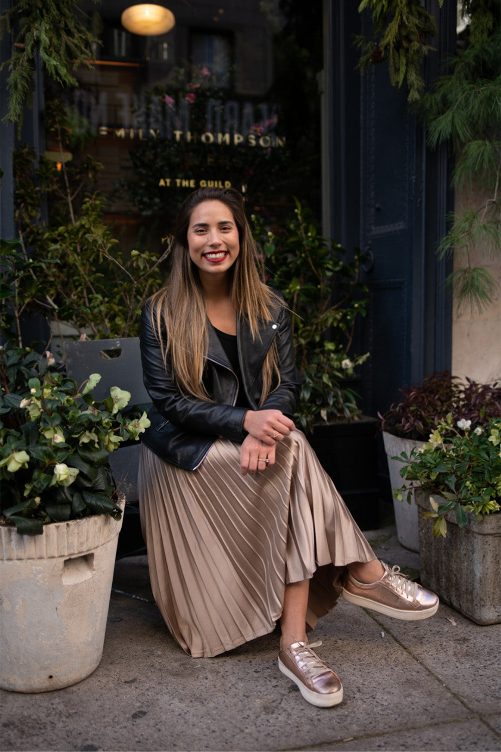 Chica sonriente sentada con las piernas cruzadas afuera de una tienda.